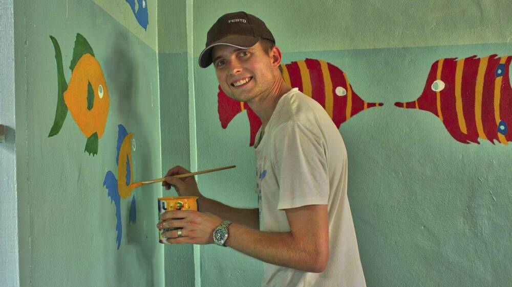 ARTISTIC: Ben Maxwell paints a wall as part of the Asian trip.