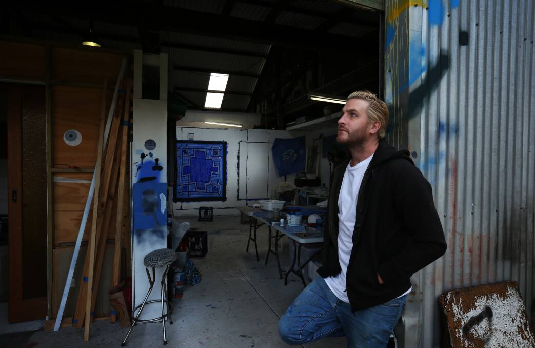 Lucas Grogan at the back of the shed, with one of his distinctive blue and white paintings on display in his studio. Picture: Simone De Peak